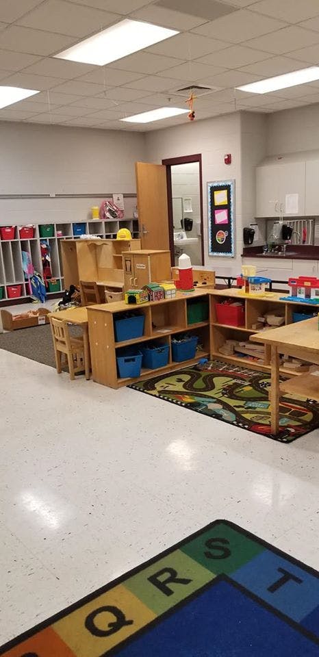 Classroom with wooden shelves, colorful bins, and a play rug