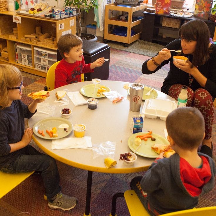 Adult and three children eating at a round table in a classroom