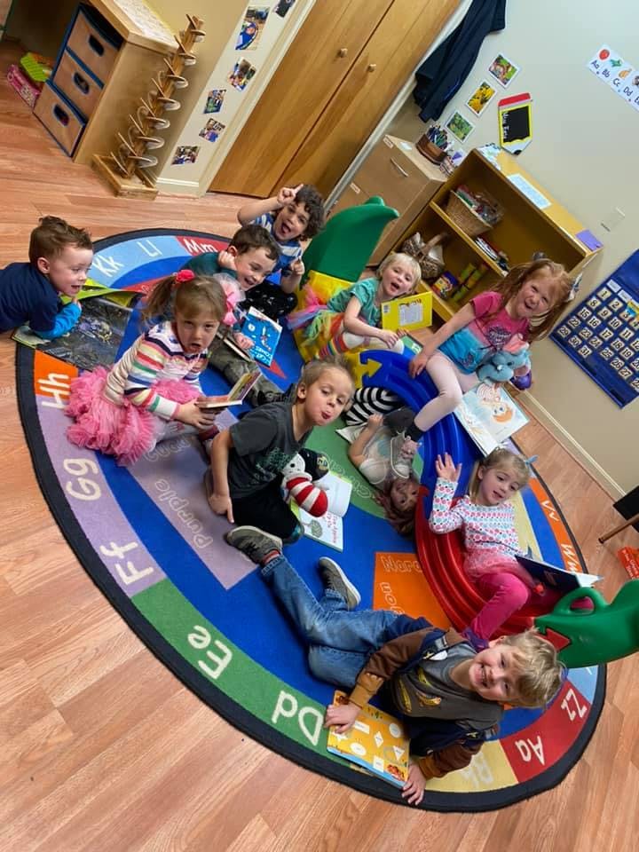 Multiple children sitting and lying on a colorful alphabet rug in a classroom