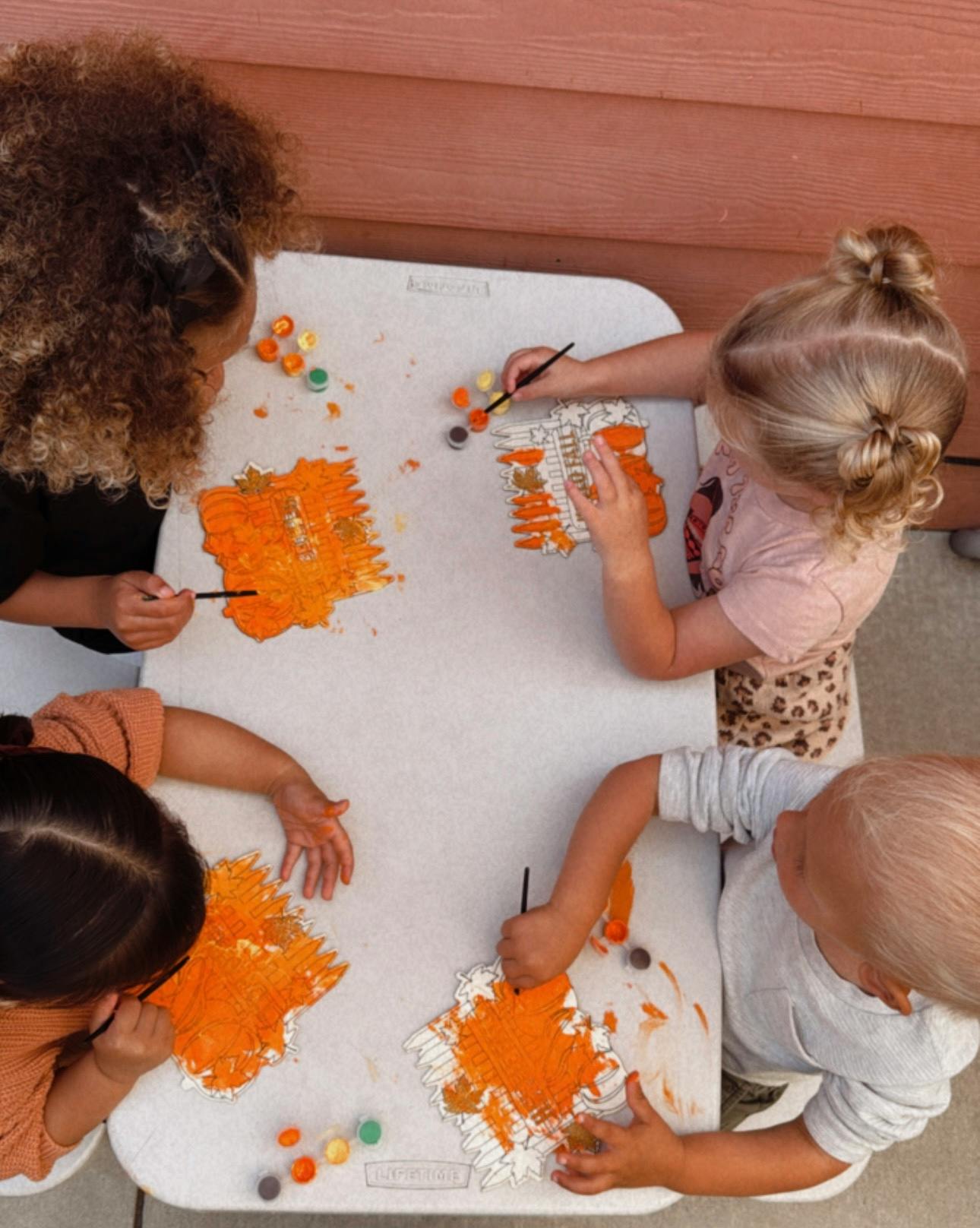 Four children painting orange shapes on a white table