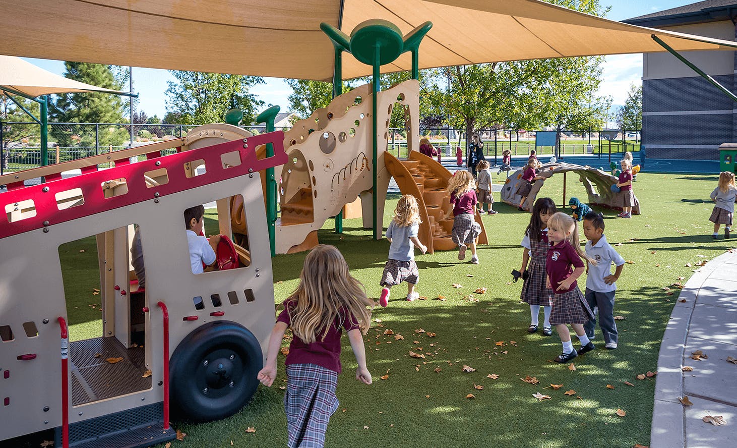 Children playing on a playground with a fire truck structure and climbing equipment