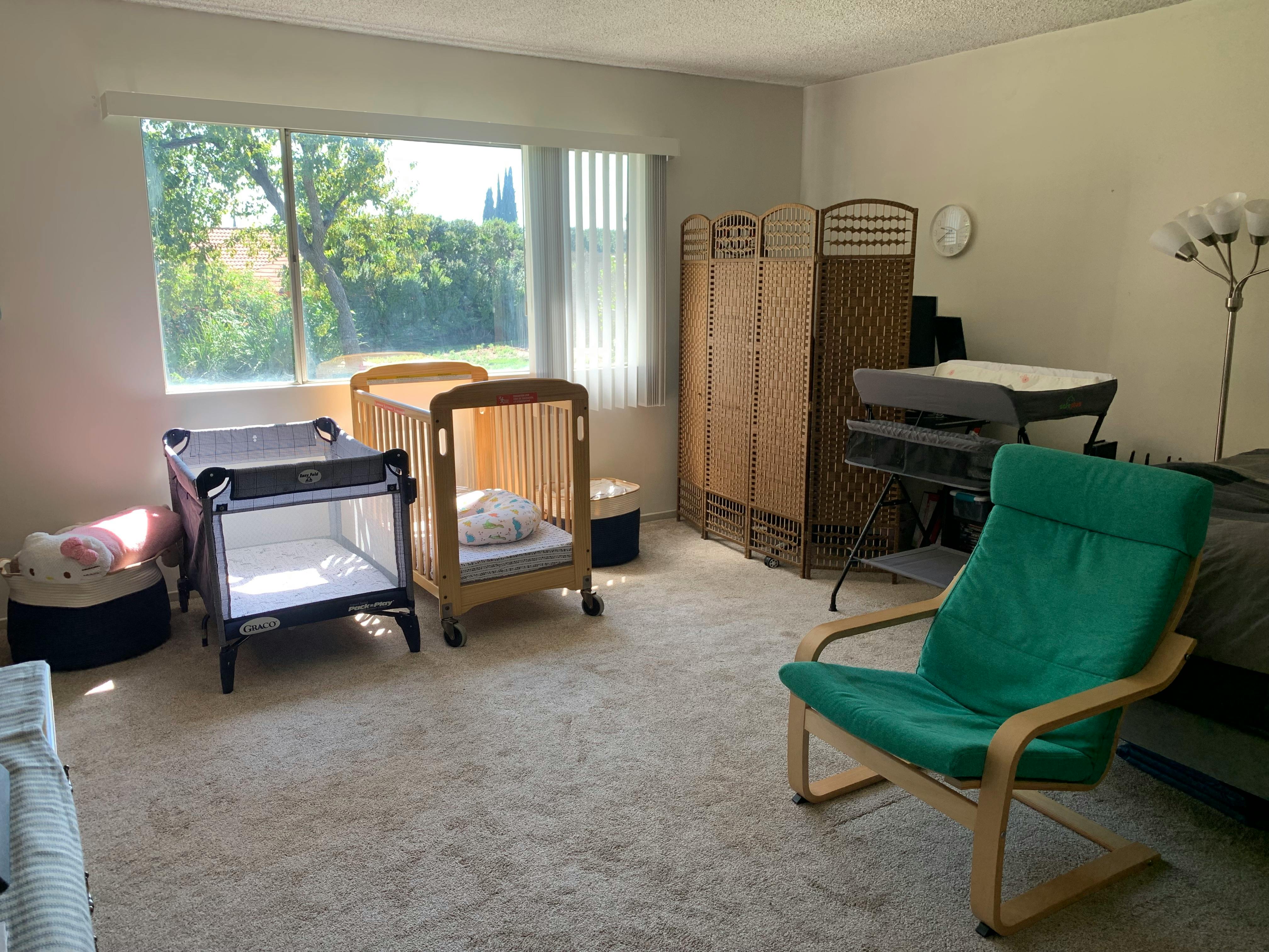 Two cribs and a green chair in a room with a large window