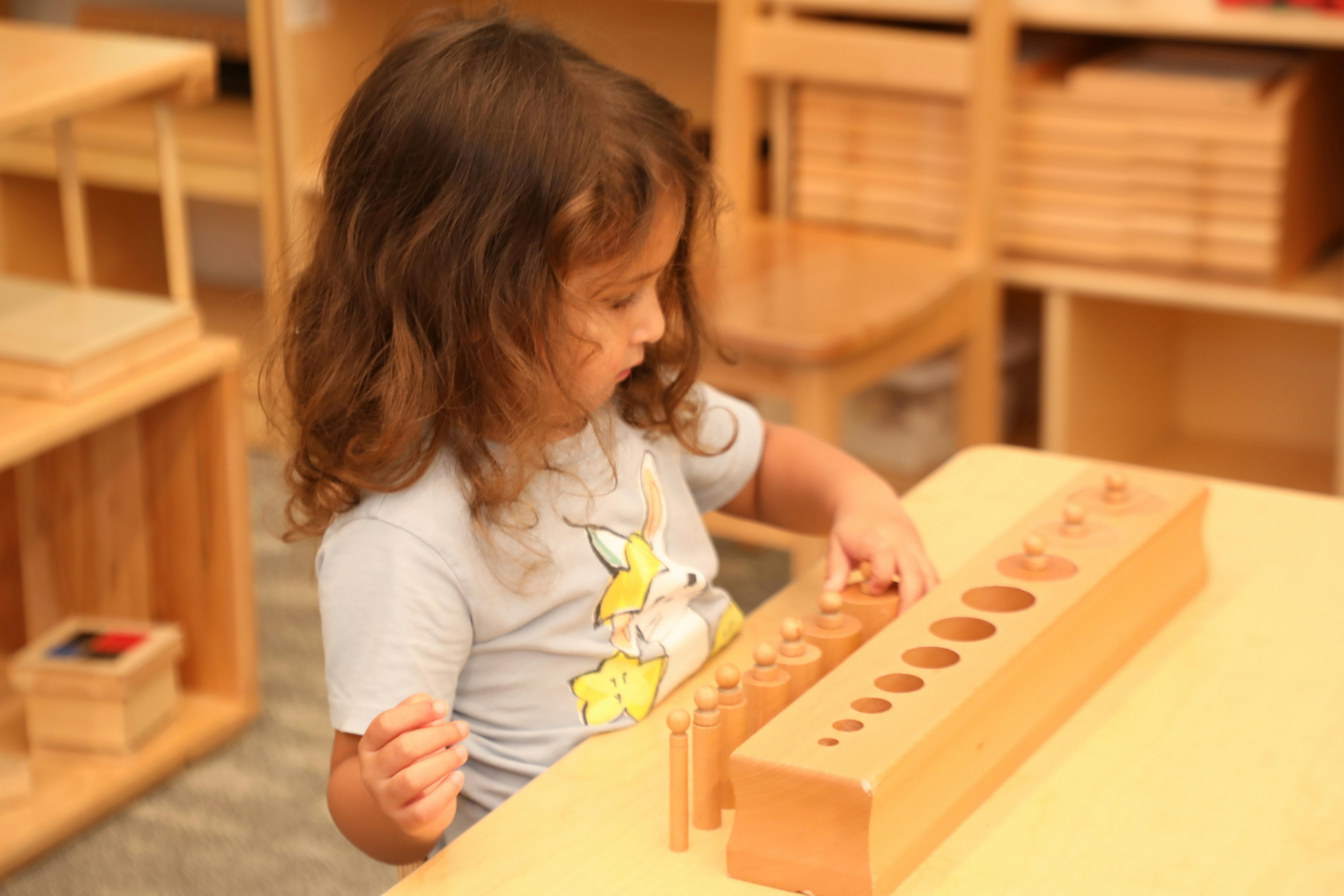 Child playing with a wooden cylinder block puzzle in a classroom