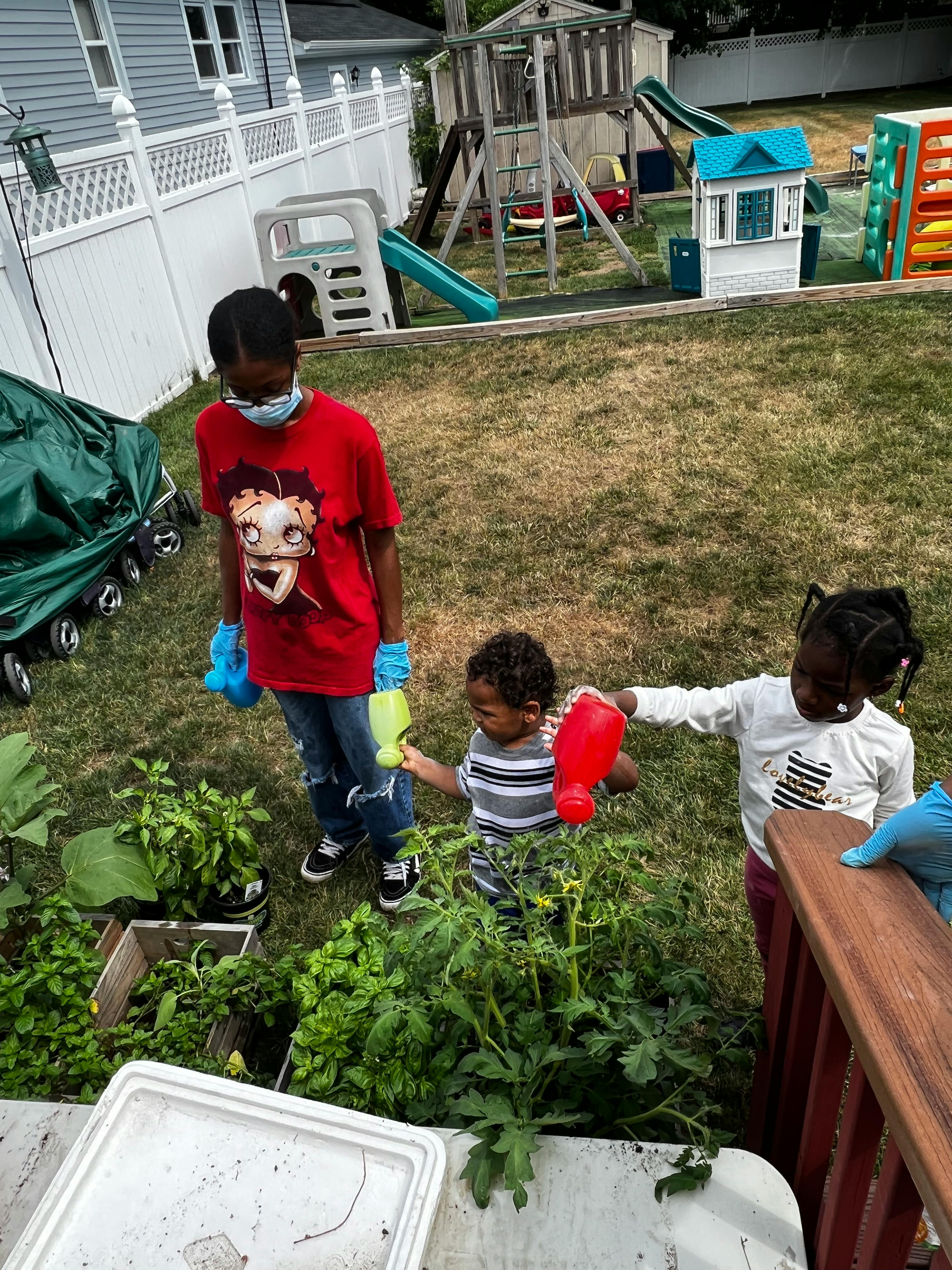 Three children watering plants in a garden