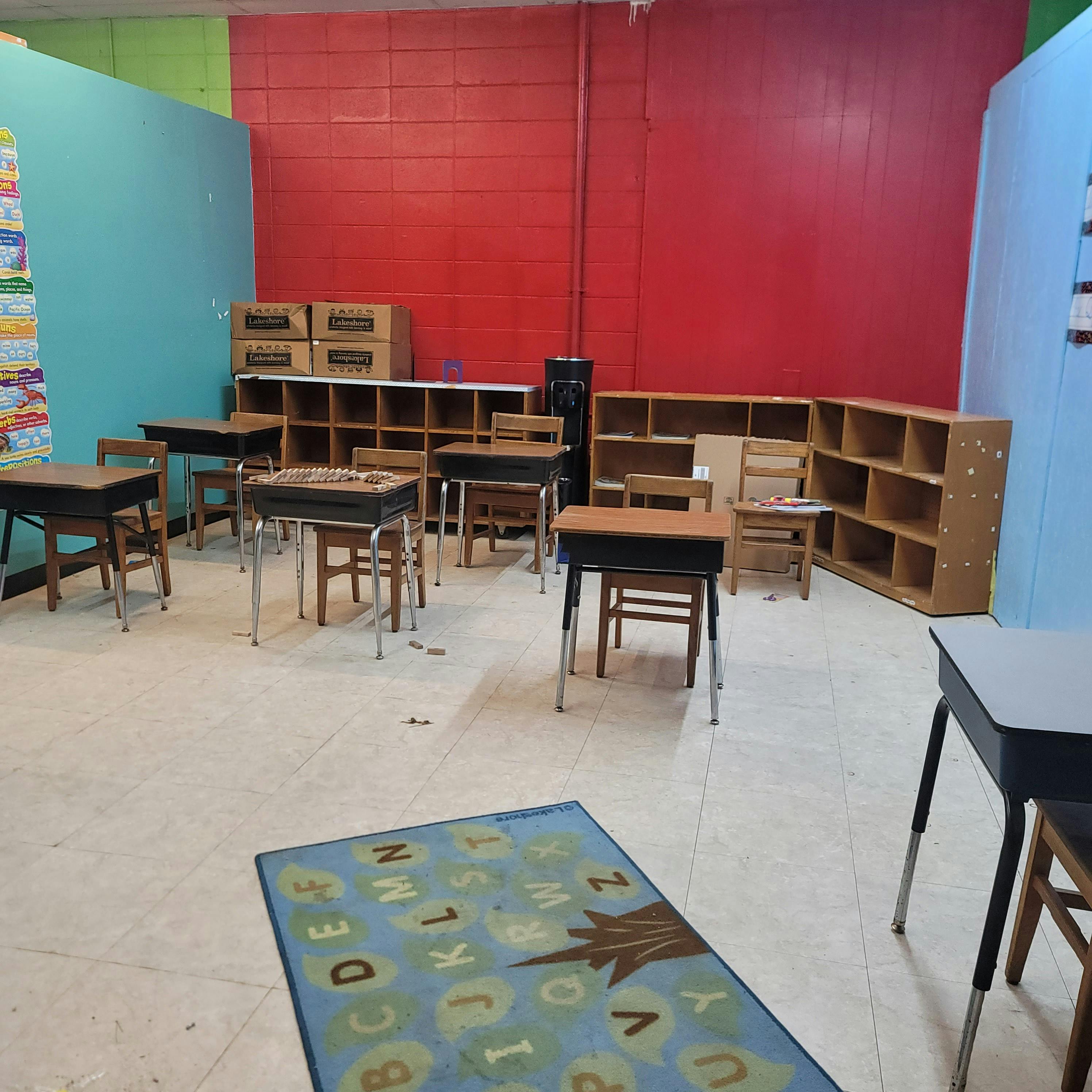 Classroom with student desks and chairs, shelves, and an alphabet rug