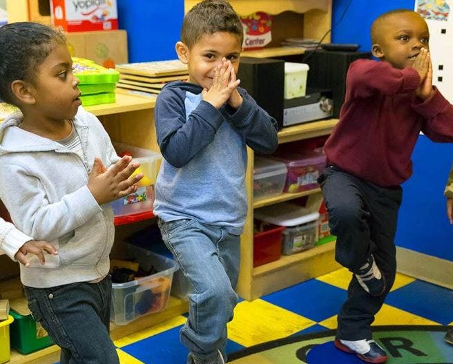 Three children standing and clapping in a classroom