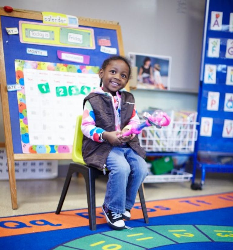 Child sitting on a chair in a classroom holding a toy