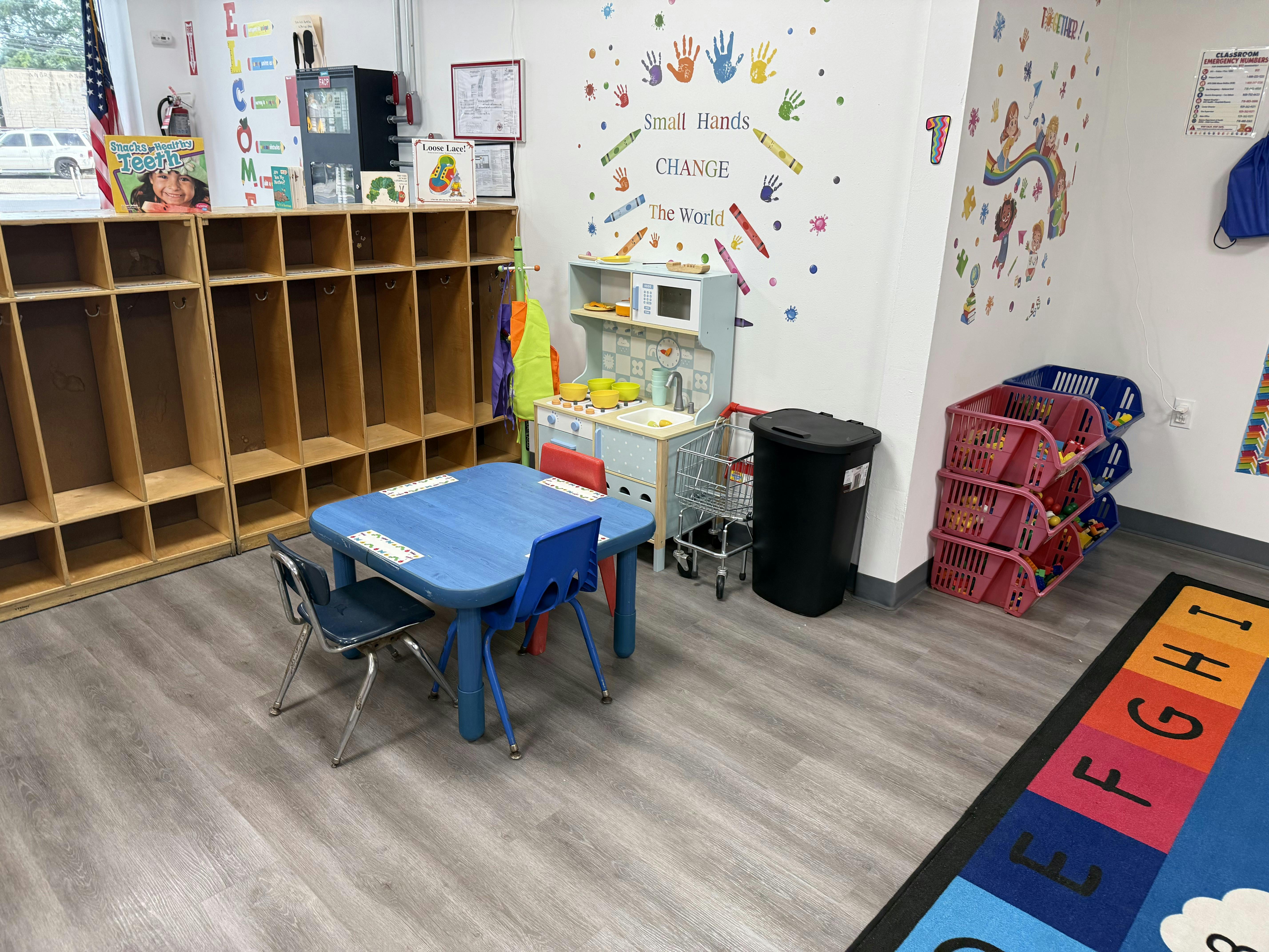 Childrens play area with a toy kitchen, small table, chairs, and storage bins