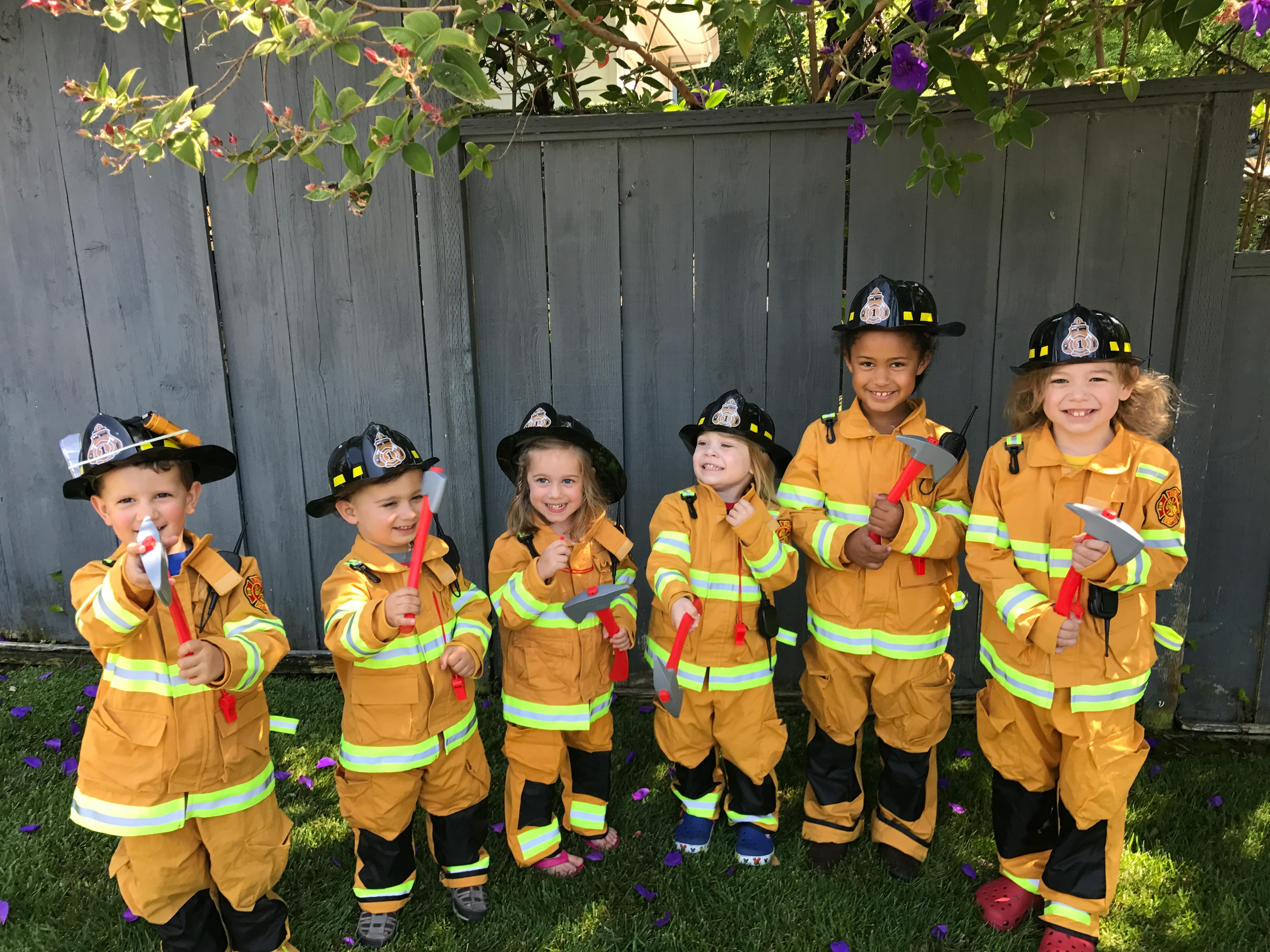 Six children in firefighter costumes holding toy axes