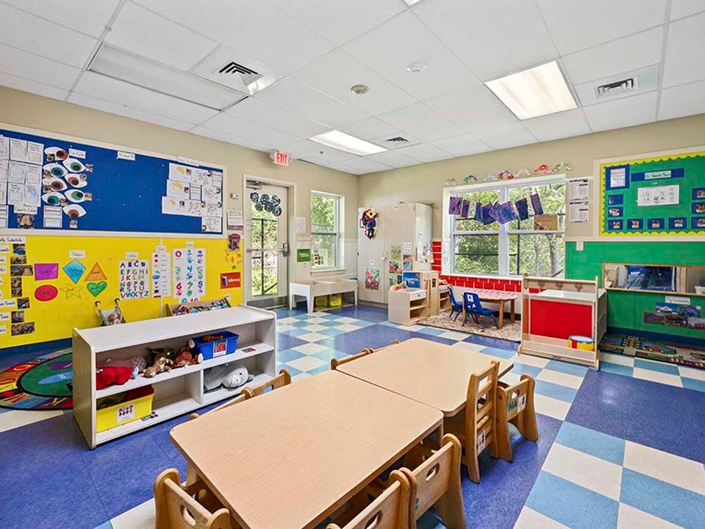 Colorful preschool classroom with small tables and chairs, toys, and bulletin boards