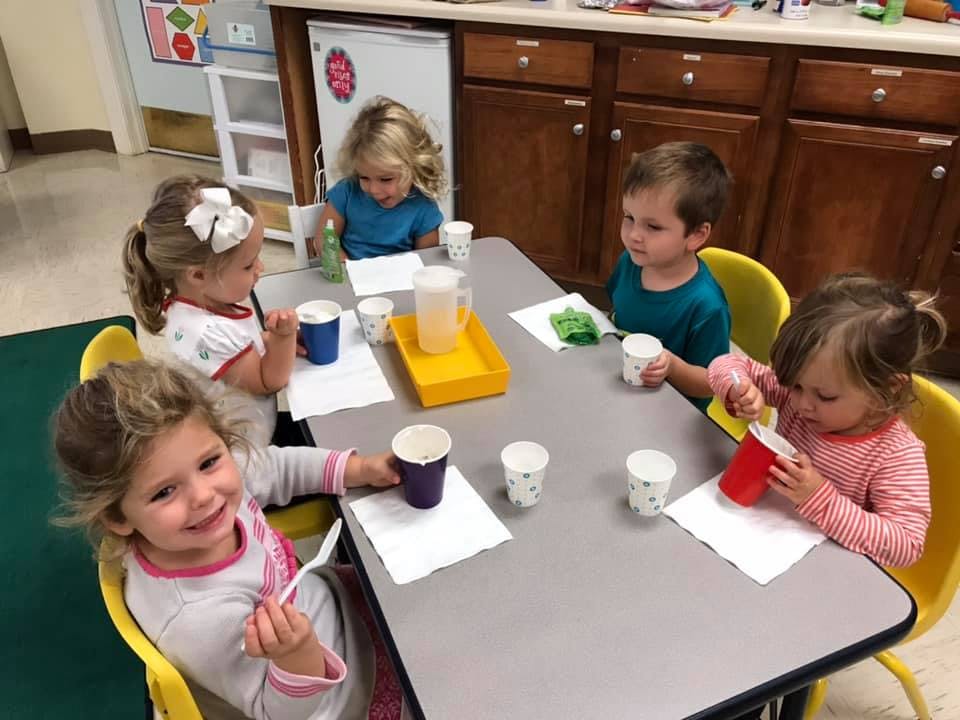 Children sitting at a table with cups and pitchers