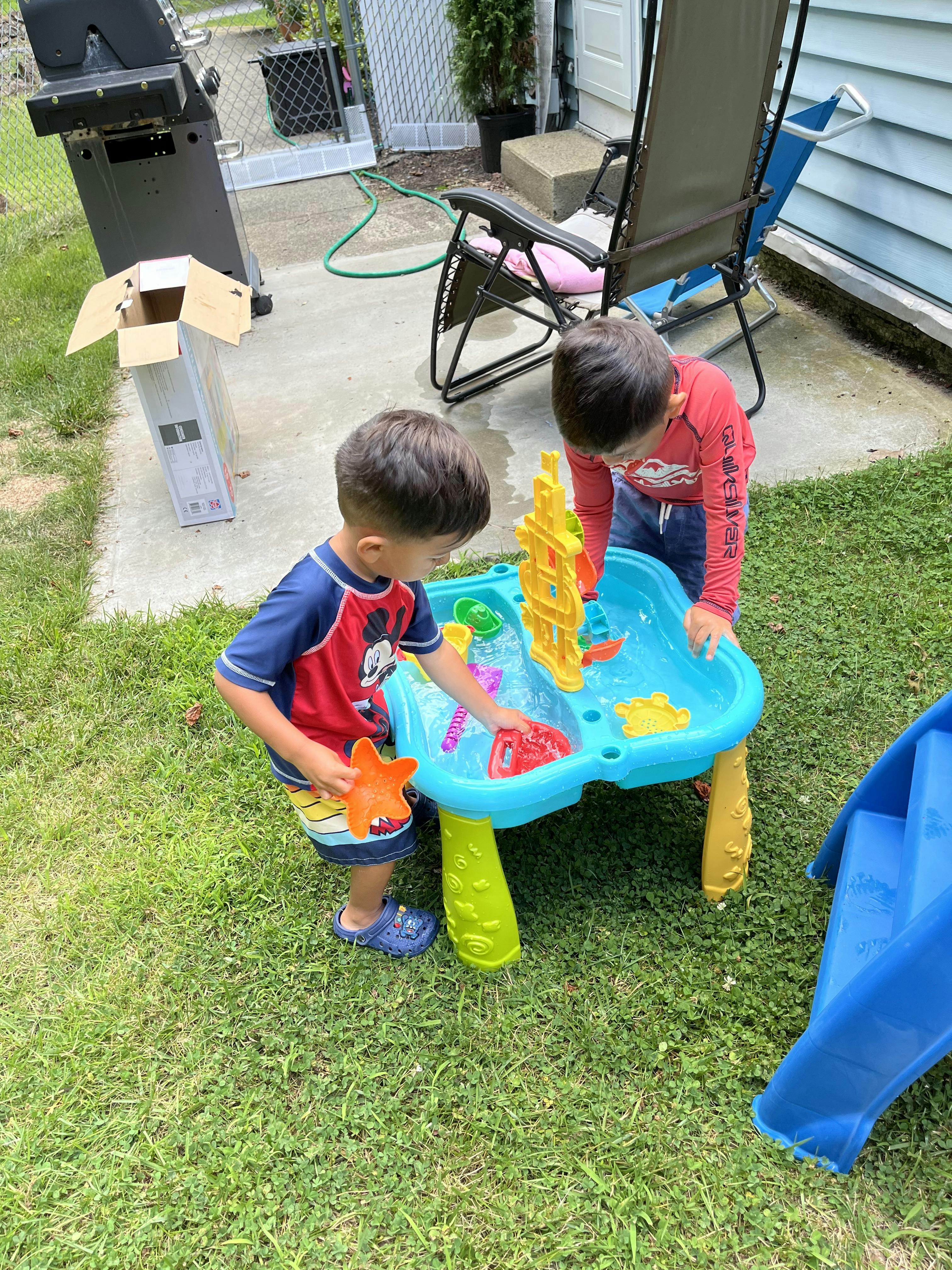 Two children playing with a water table outdoors