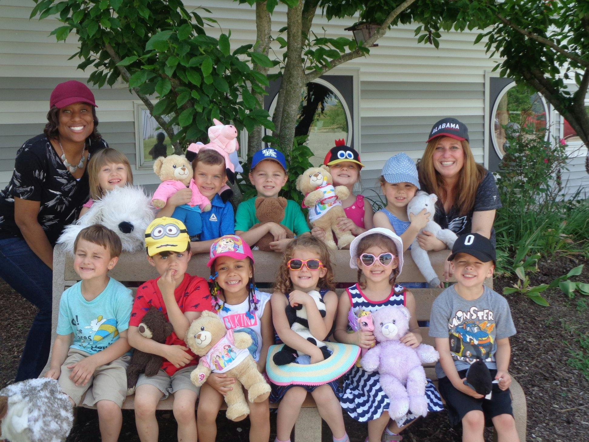 Two adults and multiple children sitting on a bench with stuffed animals