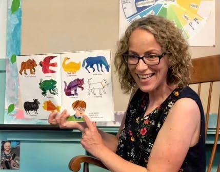 Person in glasses pointing to a children's book with animal illustrations