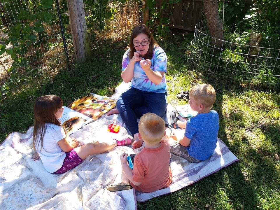 Person sitting on a blanket with three children outdoors