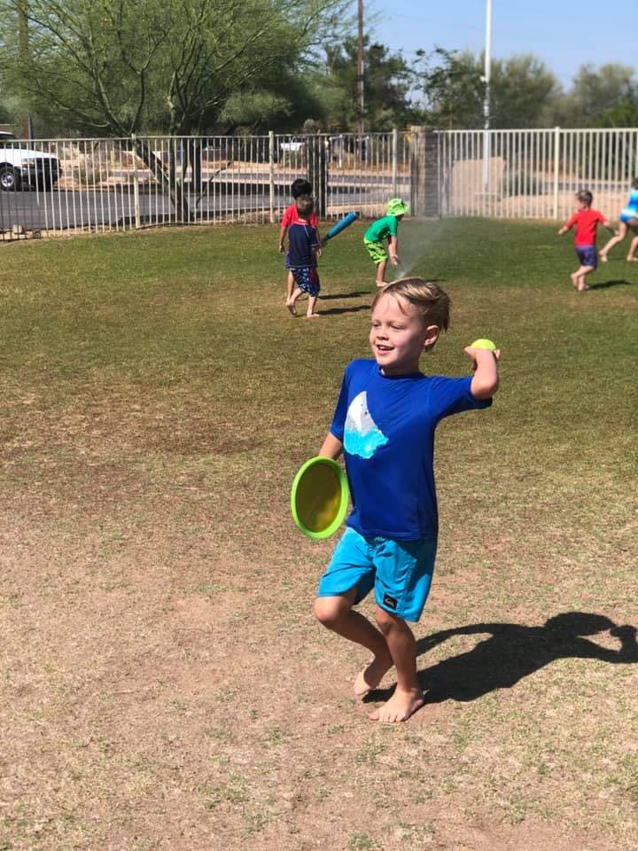 Child in blue shirt and shorts holding a frisbee and a ball