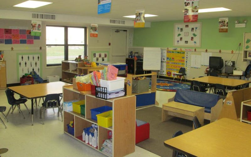 An empty classroom with light green walls and multiple tables and chairs