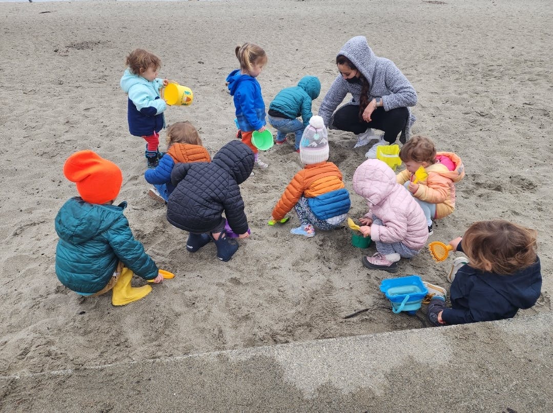 Adult and multiple children playing in sand with toys