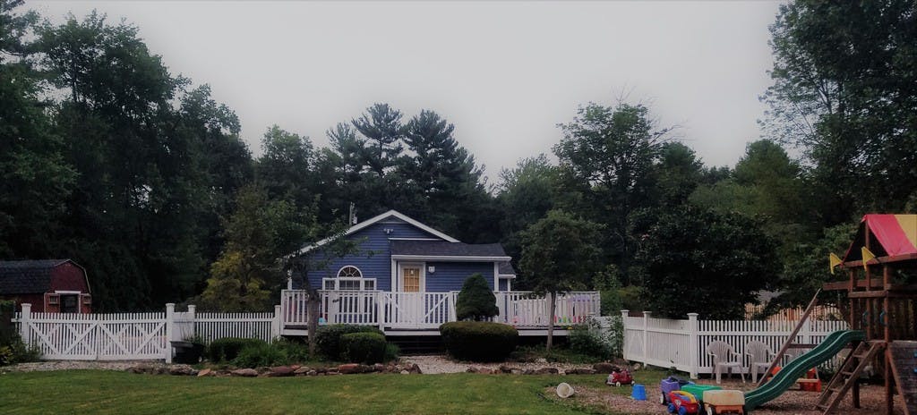 Blue house with white porch and fence, surrounded by trees
