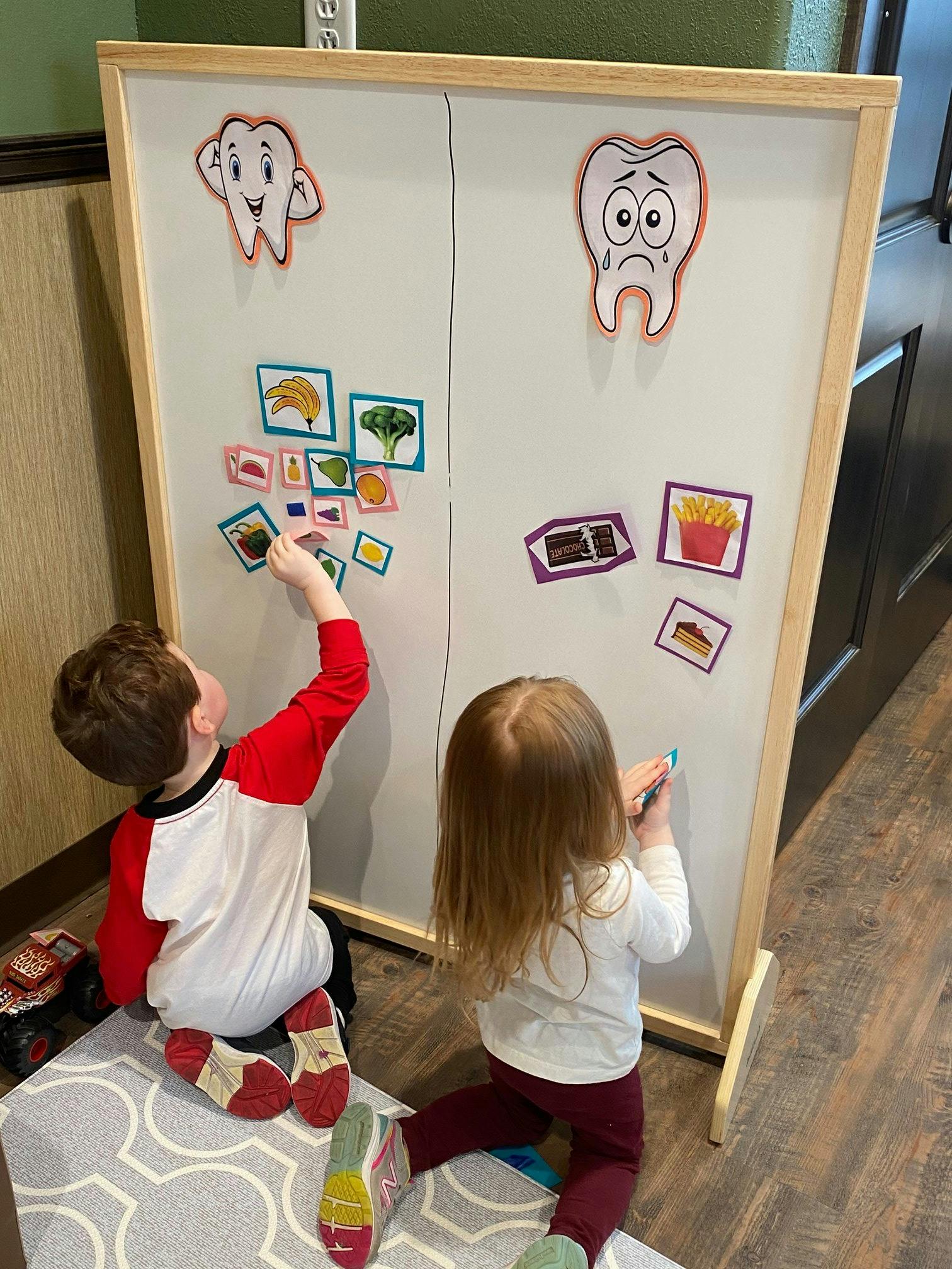 Two children playing with magnets on a whiteboard, one placing a magnet