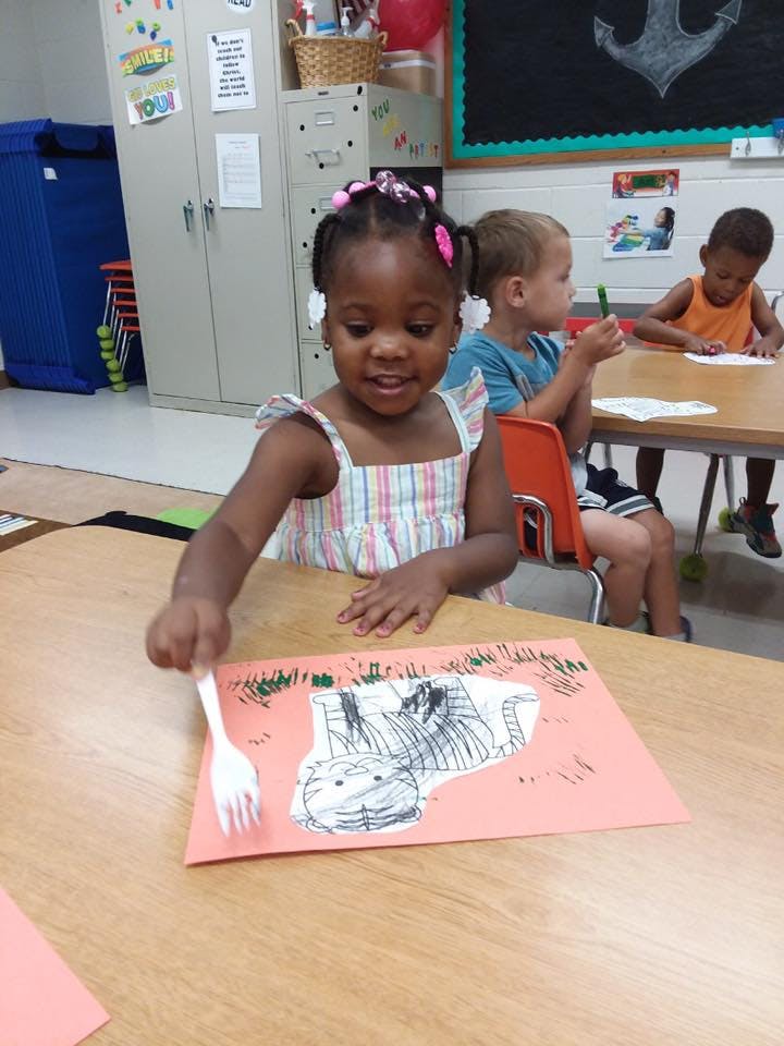 Child at a table with a drawing and a fork