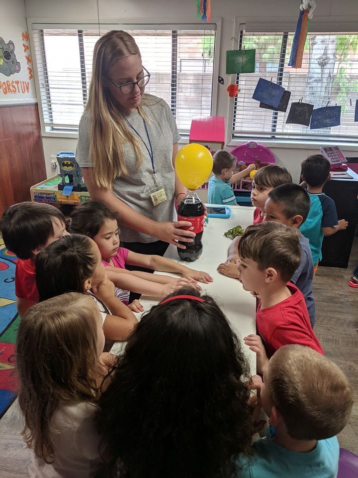 Person demonstrating a science experiment with a balloon and bottle to children