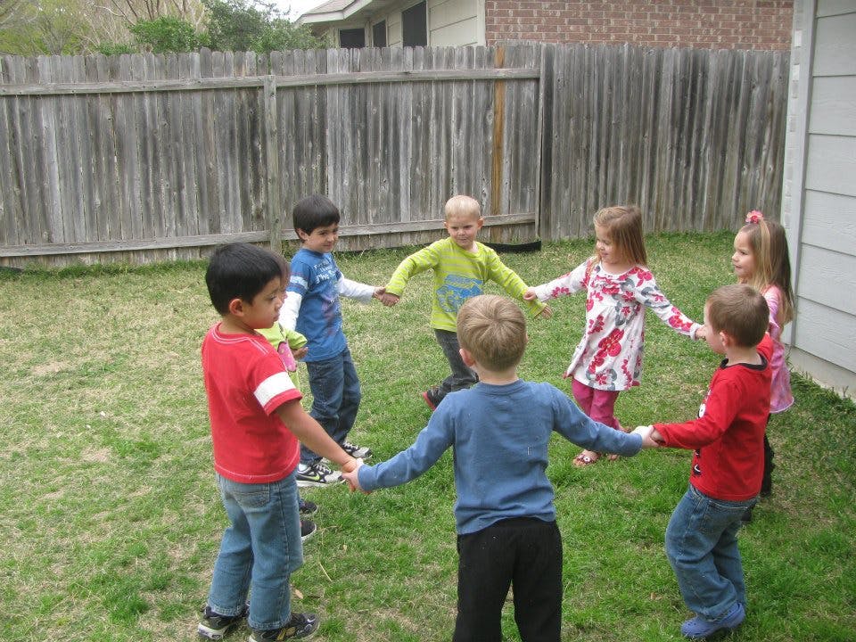 Six children holding hands in a circle on grass