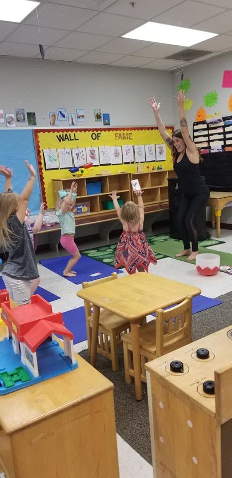 Adult and children with arms raised in a classroom