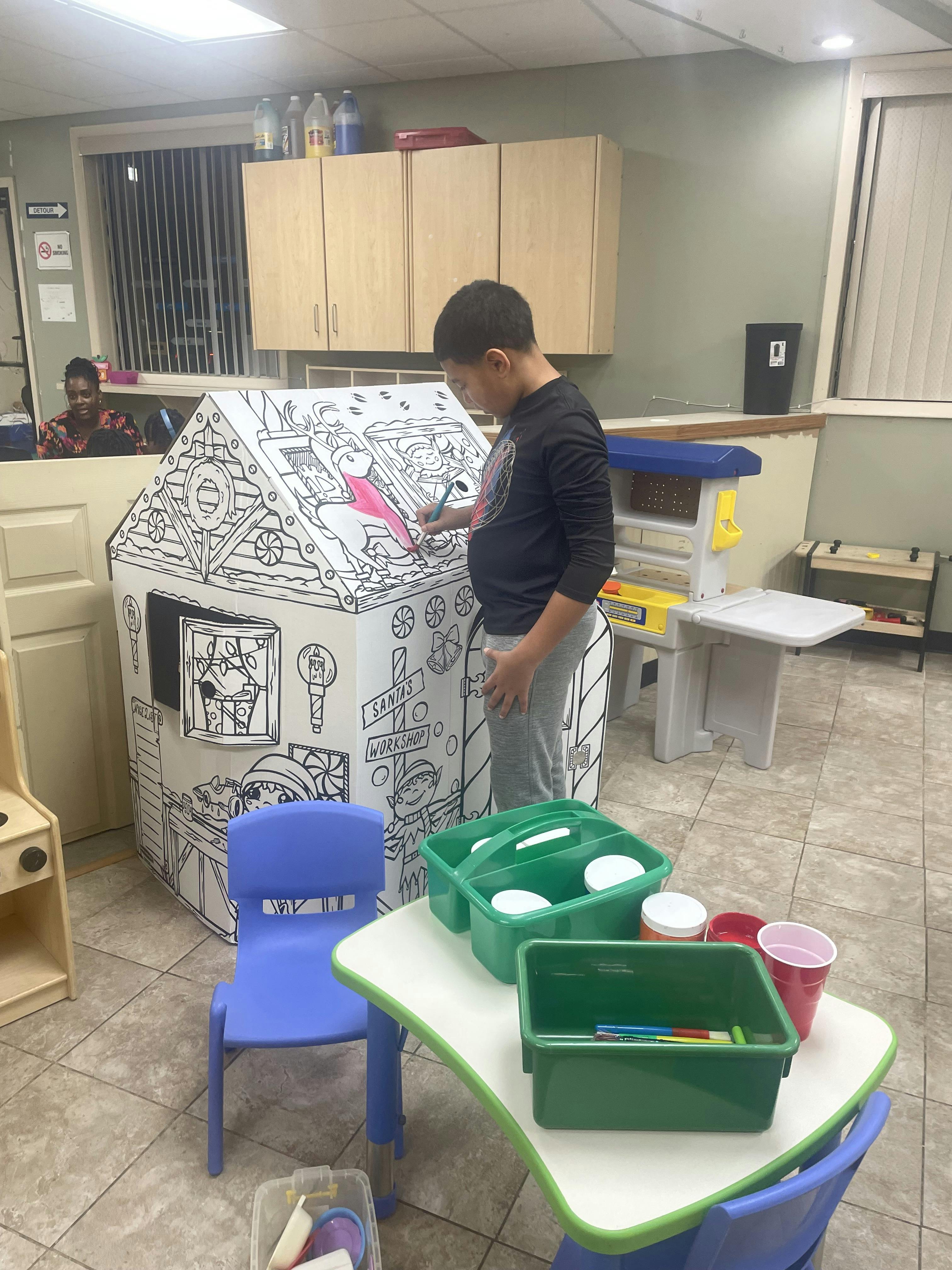 A person coloring a cardboard Santa's workshop playhouse
