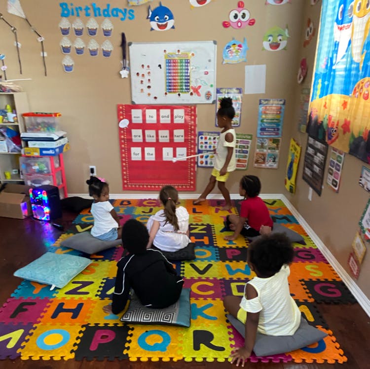 Children sitting on alphabet mat while one child points to a chart