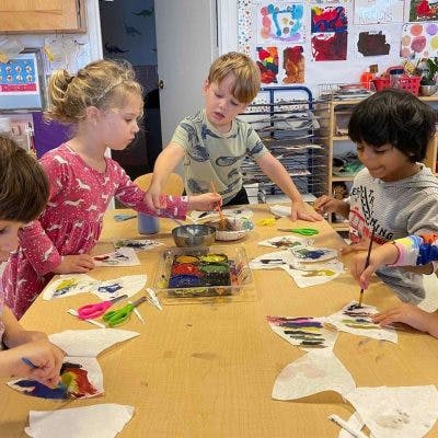 Children painting coffee filter art at a table in a classroom