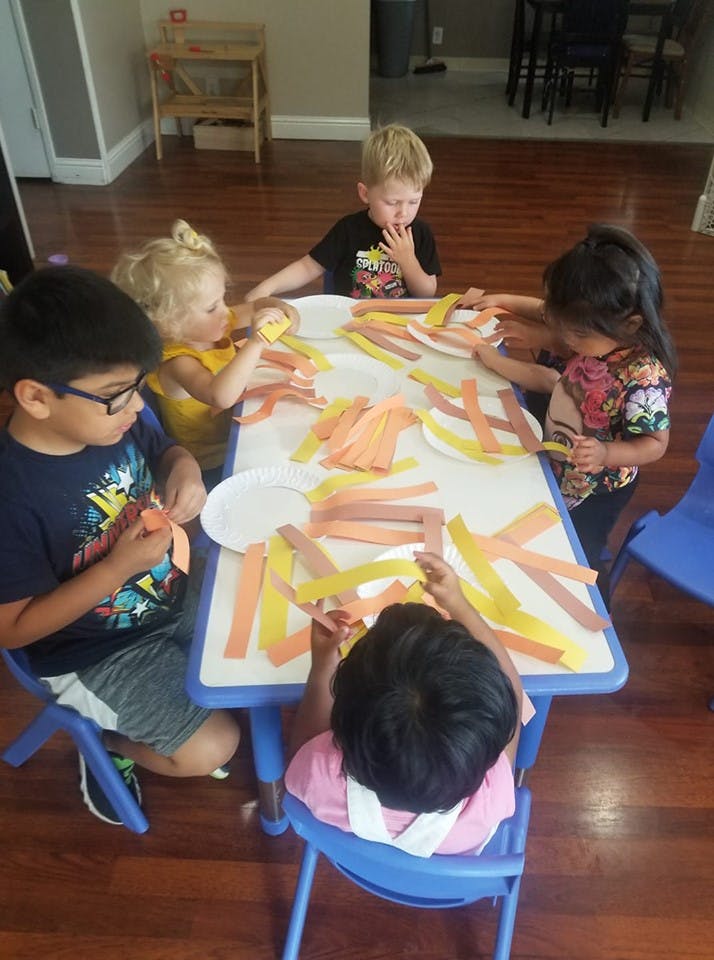 Children sitting at a table doing crafts with paper strips