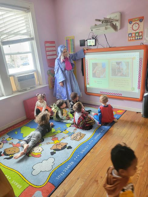 A person in a costume pointing to an interactive whiteboard for a group of children