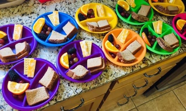 Multiple colorful plates with sandwiches, fruit, and cheese