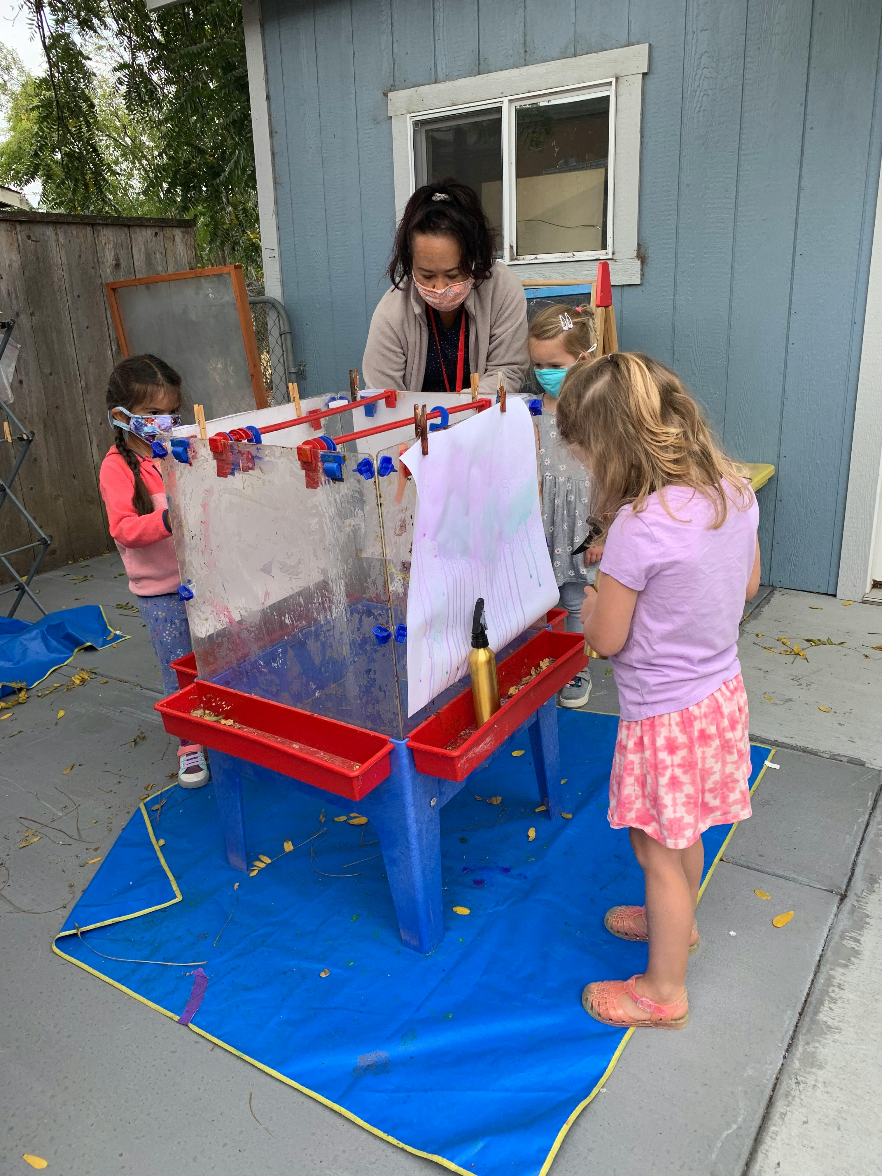 Adult and children painting at an easel outdoors