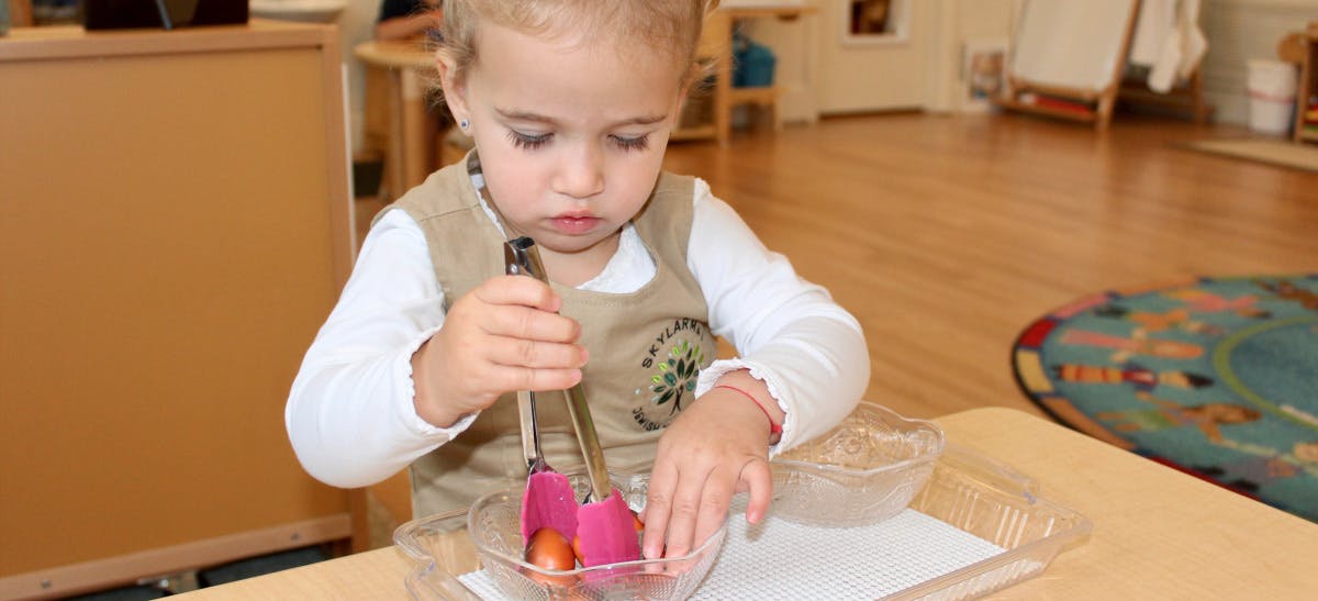 Child using tongs to pick up items from a bowl