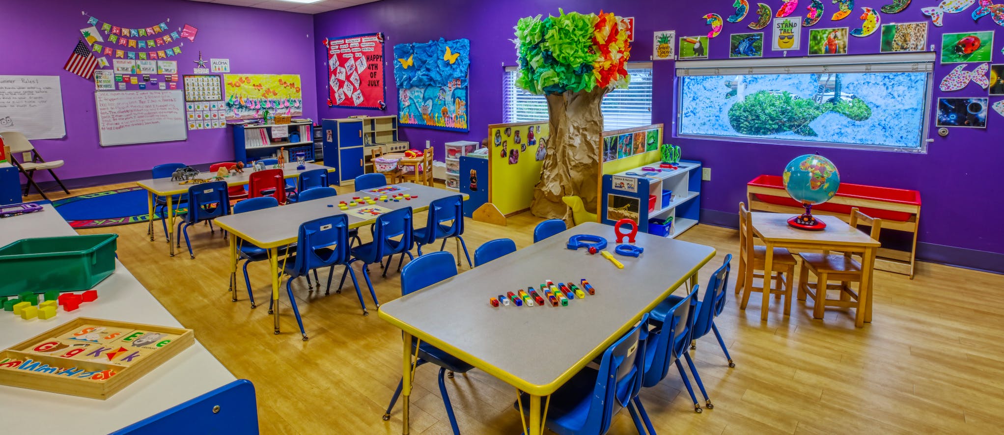 A classroom with several tables and blue chairs, educational decorations on purple walls
