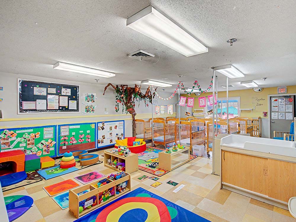A childcare classroom with cribs, play mats, and learning displays