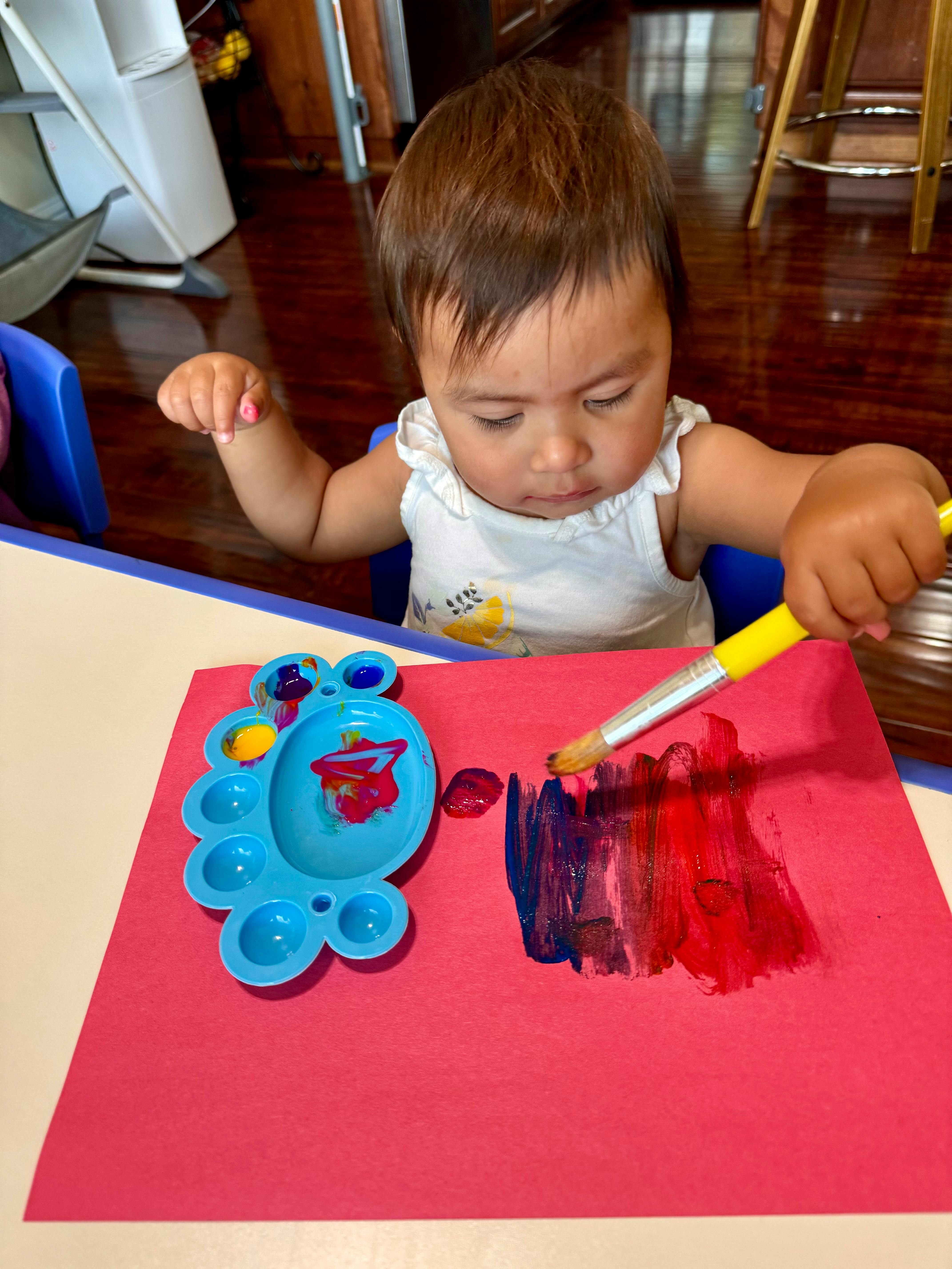 Child painting on red paper with a paintbrush and paintbrush