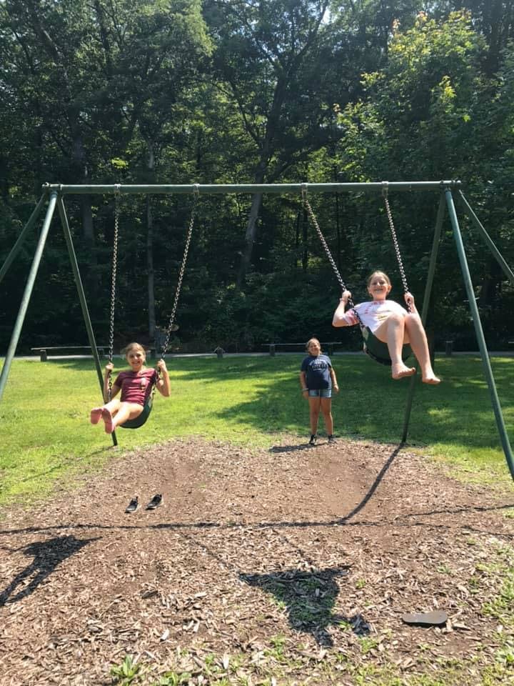 Two children swinging on a swing set, another child standing nearby