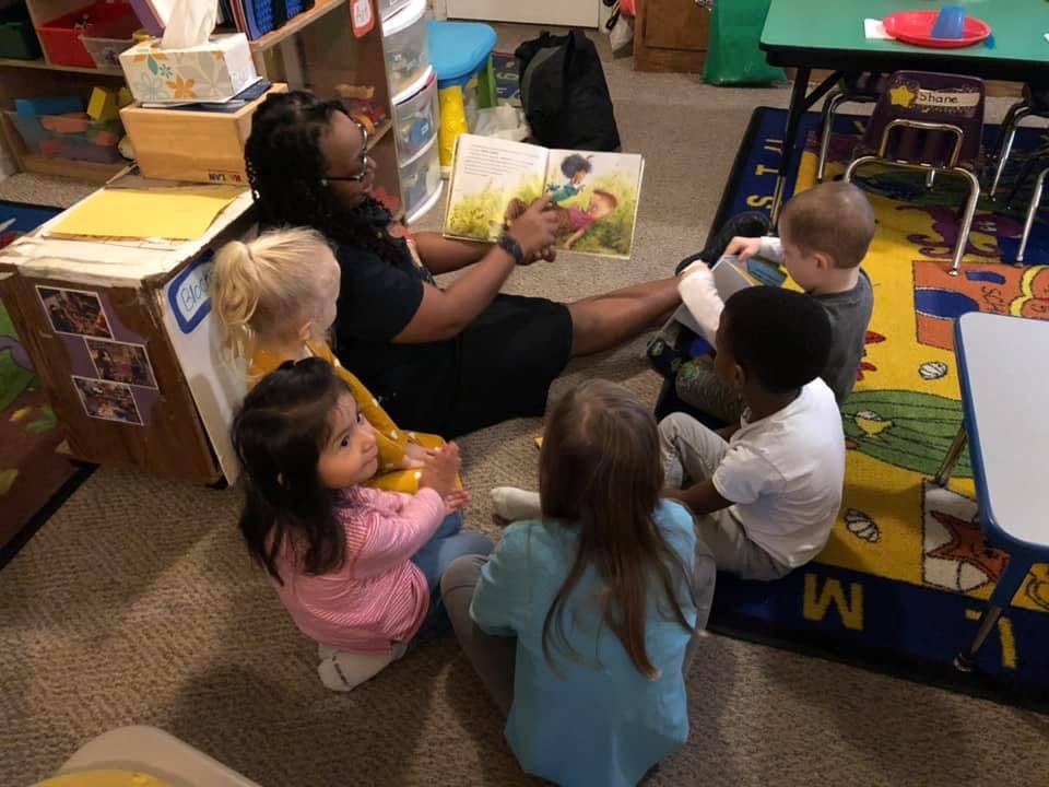 Person reading a book to a group of children in a classroom