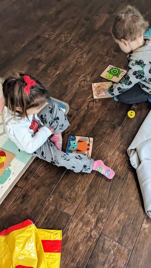 Two children playing with puzzles on a wooden floor