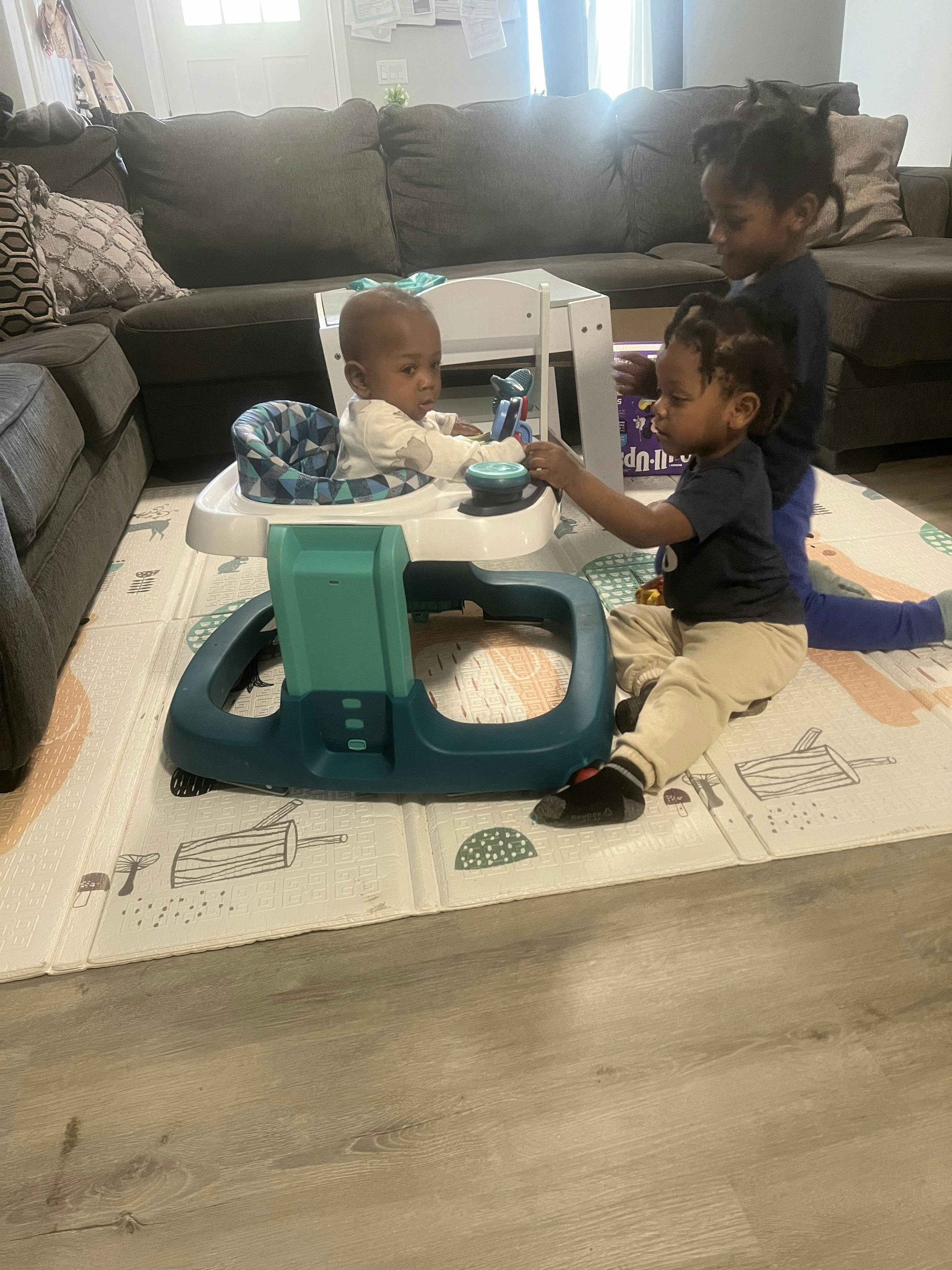 Three children playing on a mat, one in a walker