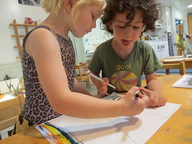 Two children drawing on paper with markers