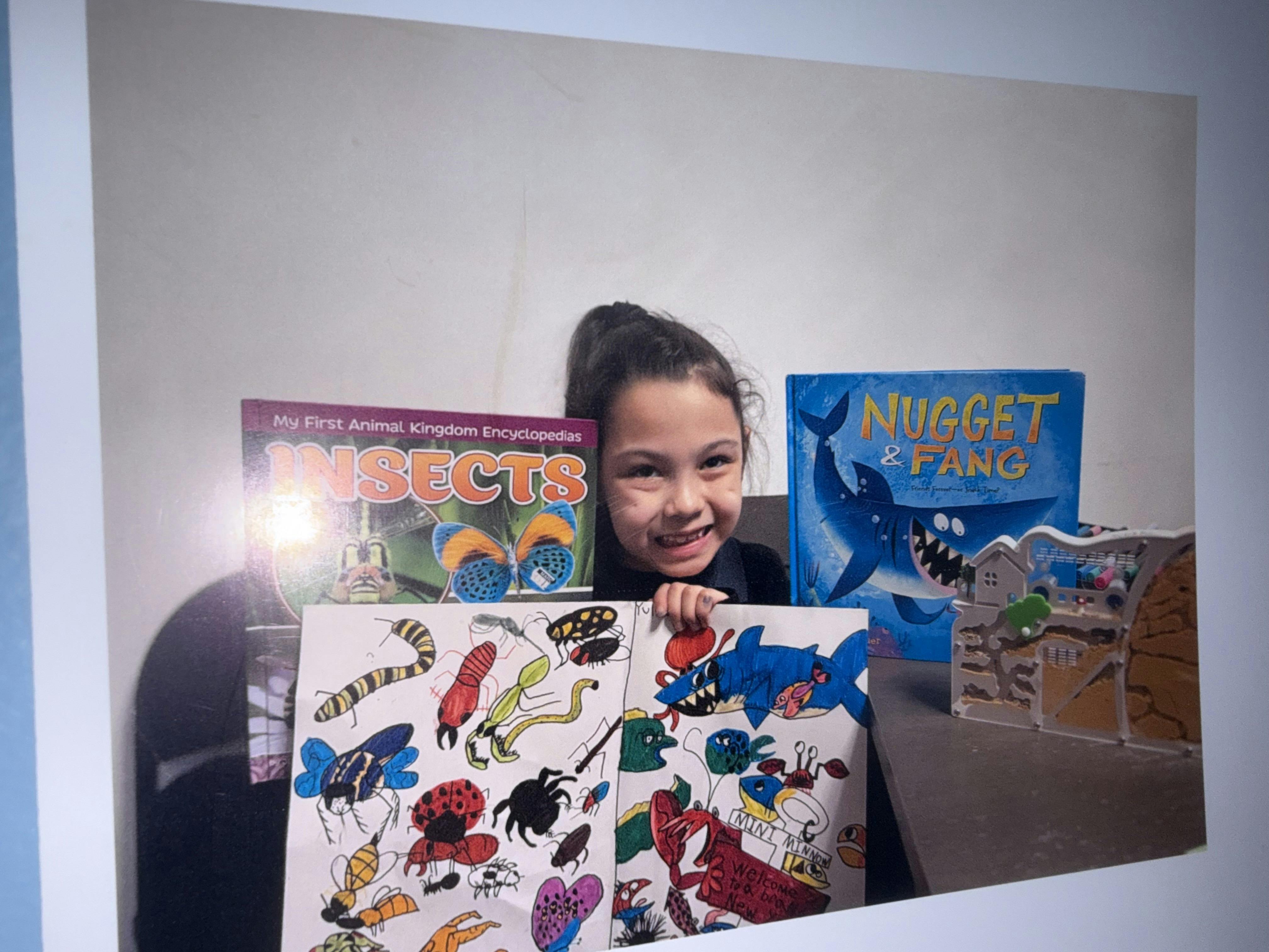 Child holding illustrated posters alongside animal and shark books