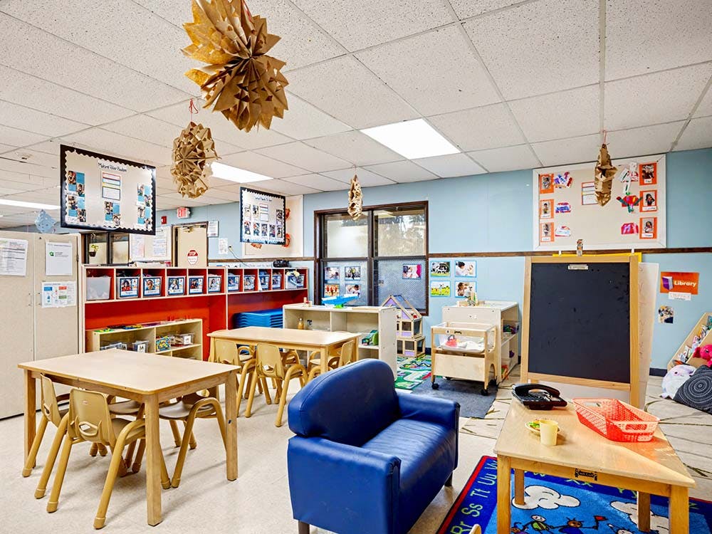 Classroom with small tables, chairs, a blue couch, and a chalkboard