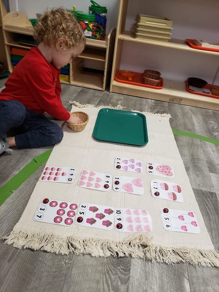 Child on floor playing with counting cards and small basket