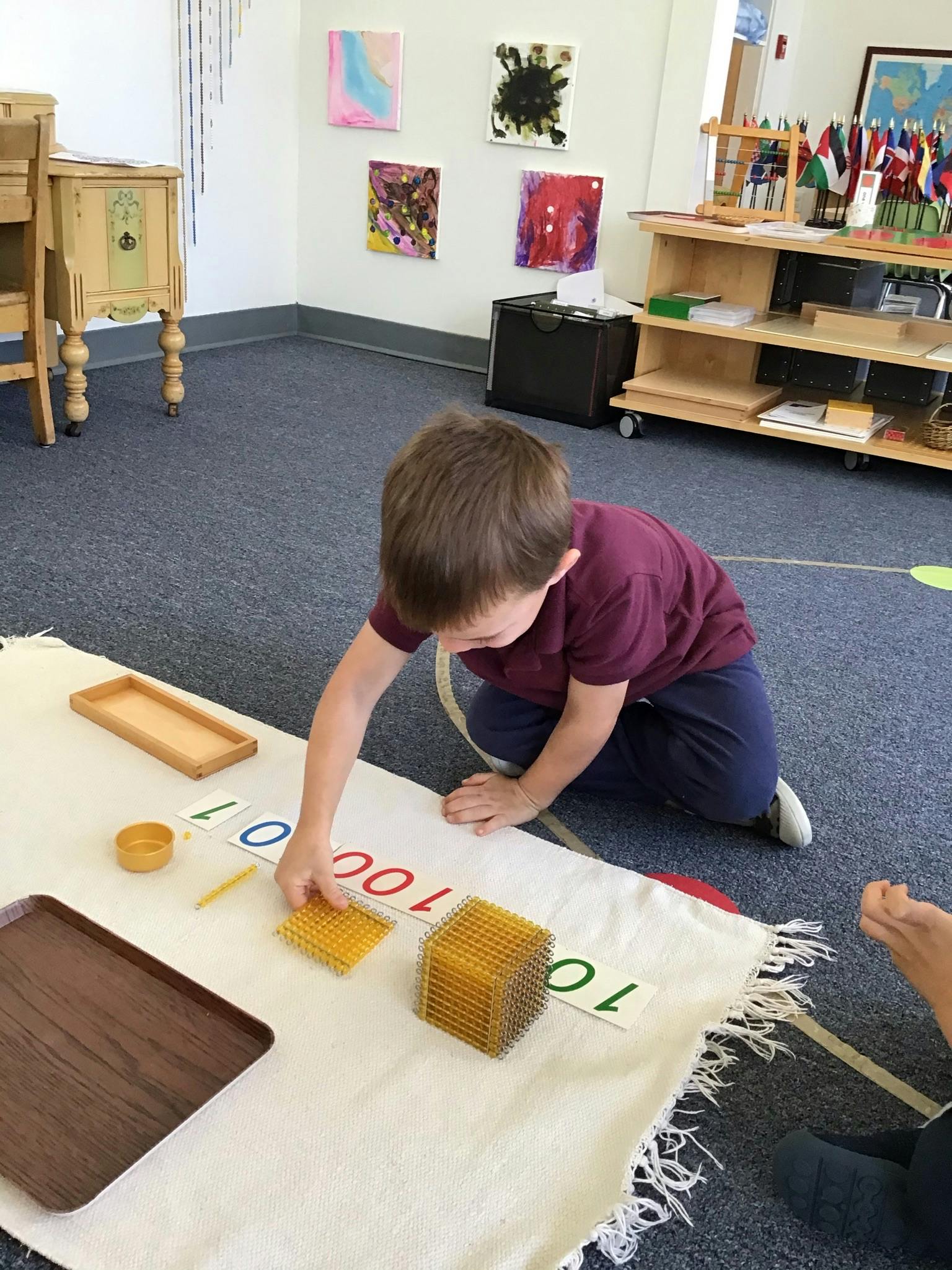 Child kneeling on floor, arranging number cards and blocks on a mat