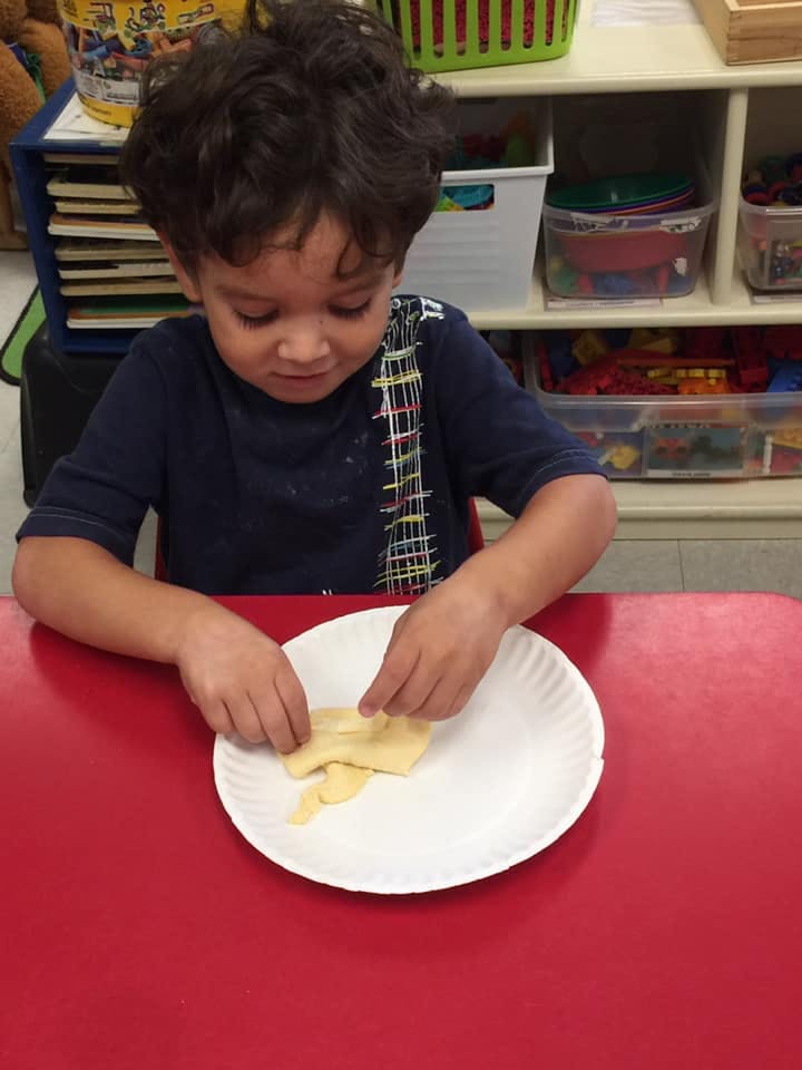 Child at a red table manipulating dough on a paper plate