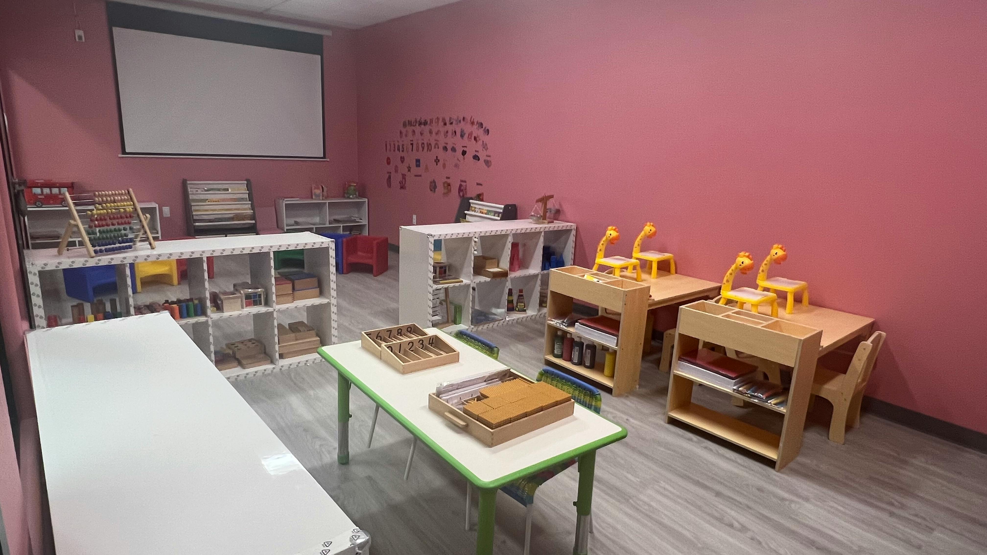 Classroom with small tables and chairs, shelves with learning materials